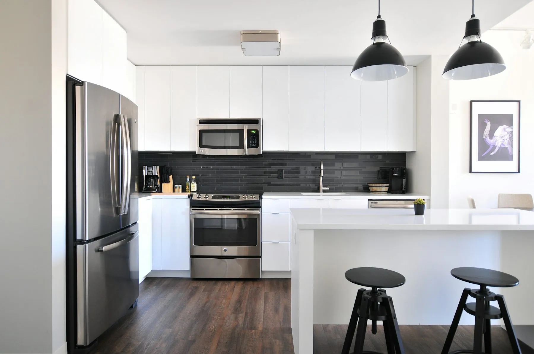 Bright white fitted kitchen with stainless steel appliances and bar stools