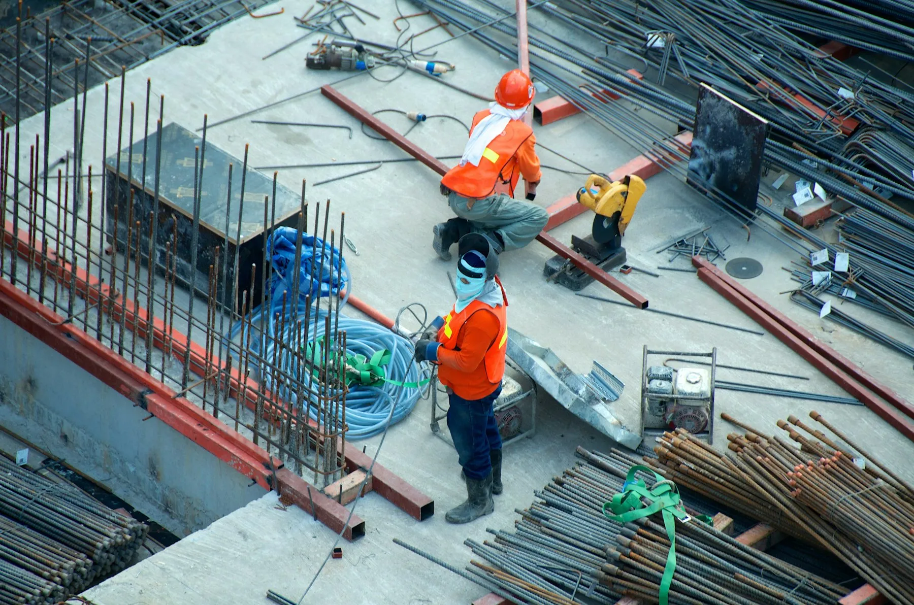 Construction workers in hard hats and hi-vis tying steel reinforcement bars on a building site