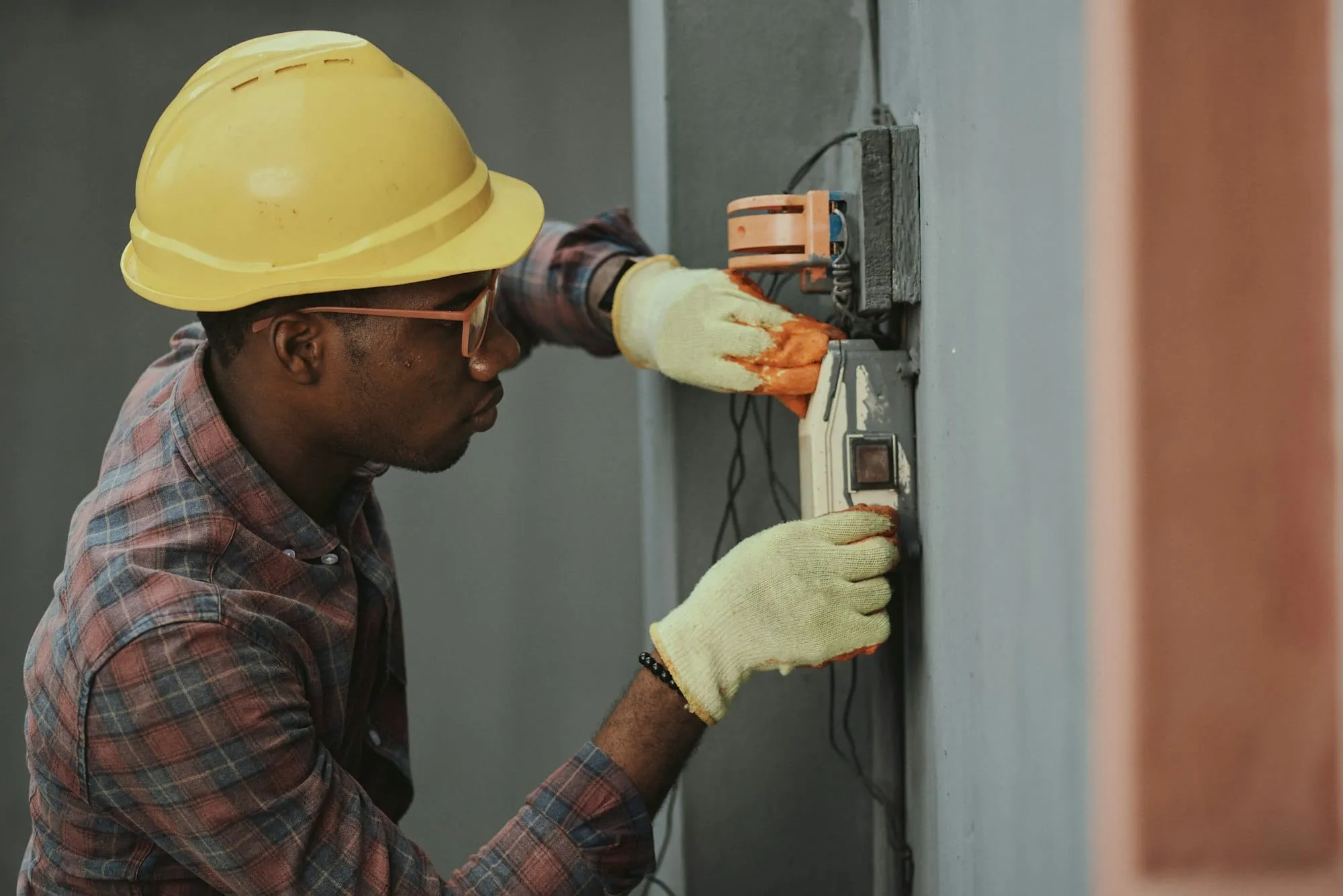 Engineer in a hard hat and gloves testing equipment on a wall