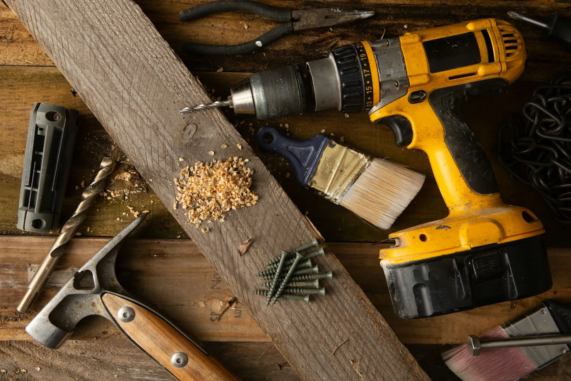 Cordless drill, hammer, screws and a paintbrush on a workbench