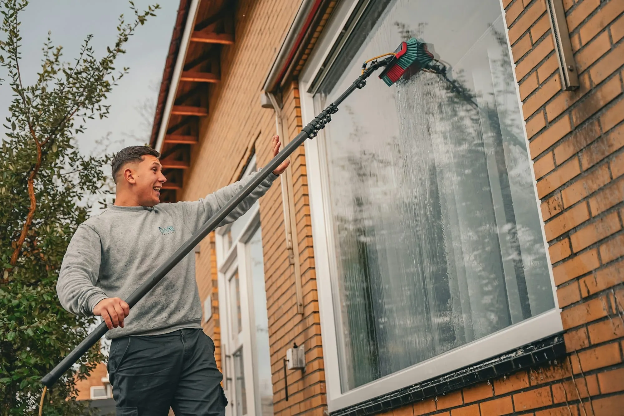 Window cleaner washing a window with a water-fed pole